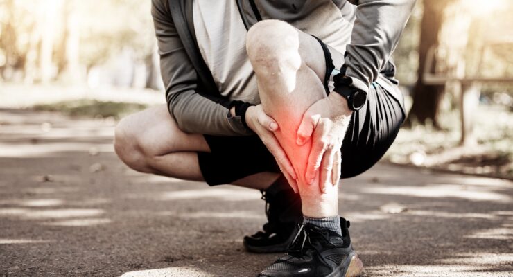 Person wearing athletic gear and shorts, squatting down and clutching their shin, which is glowing red.